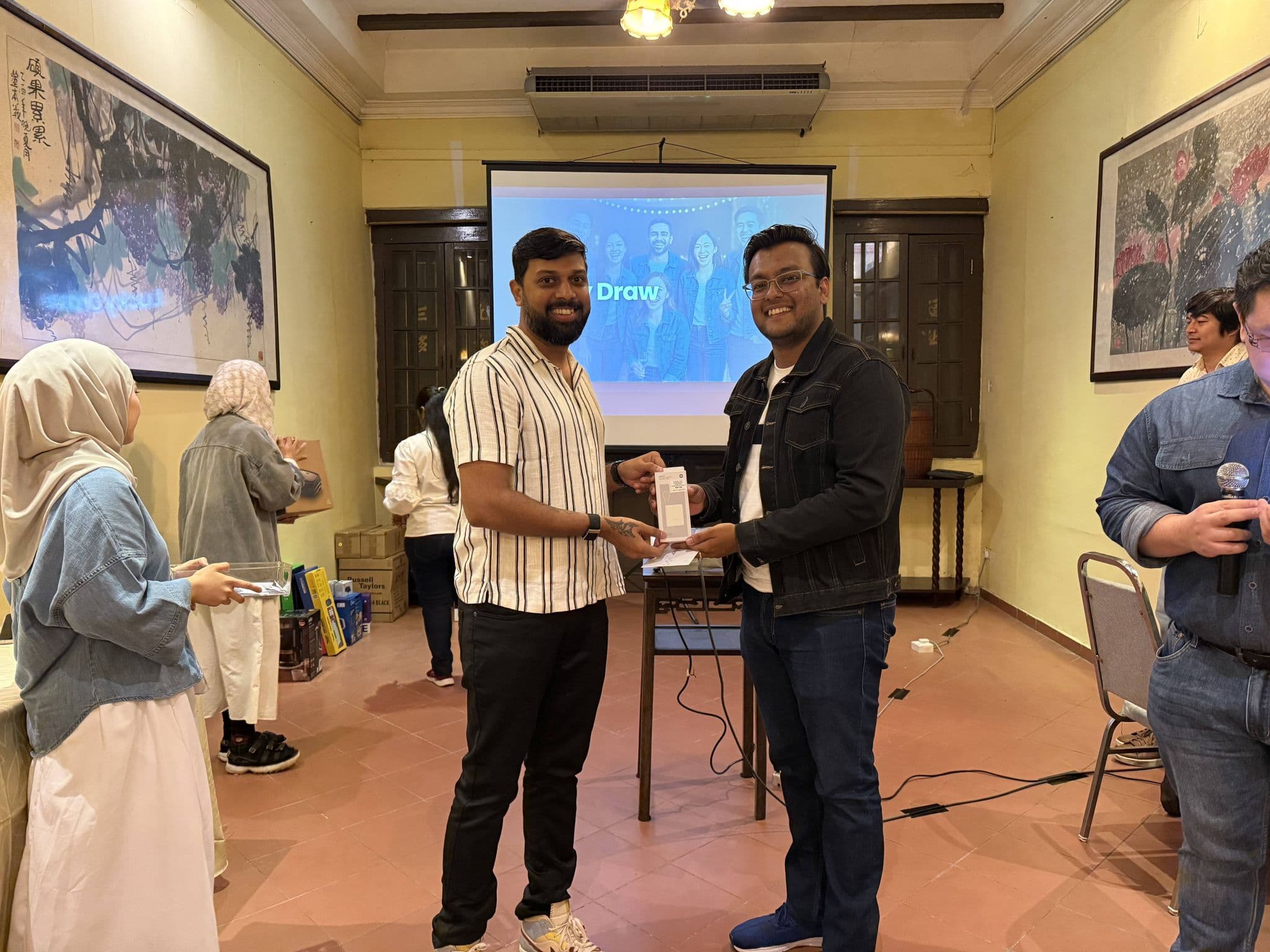Anchit Shrivastava smiling and receiving a gift from a colleague at an indoor team event.