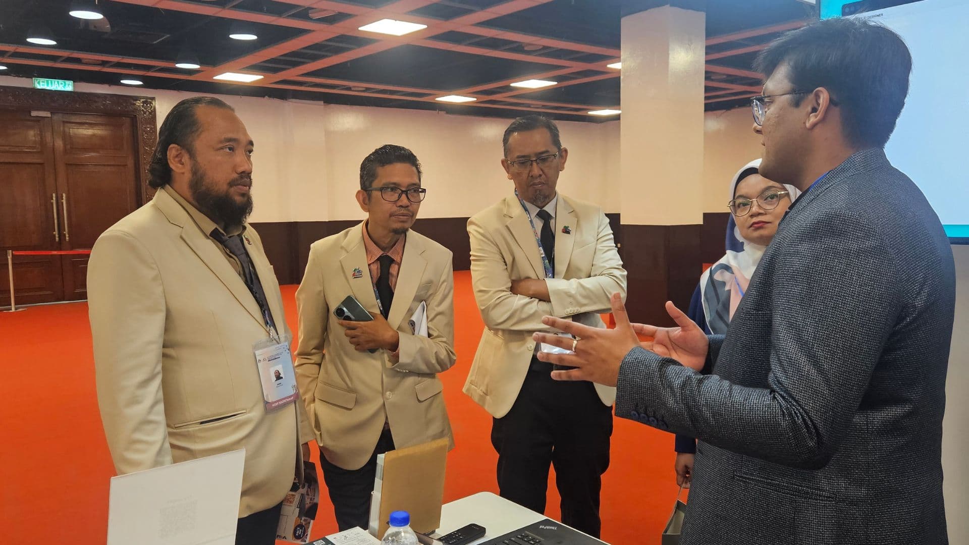 Anchit Shrivastava gesturing while explaining Joget's product to a group of delegates in blazers at the exhibition booth.